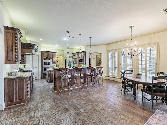 kitchen with a kitchen island with sink, decorative light fixtures, ornamental molding, and light stone countertops