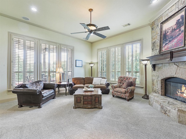 living room with crown molding, a stone fireplace, ceiling fan, and carpet