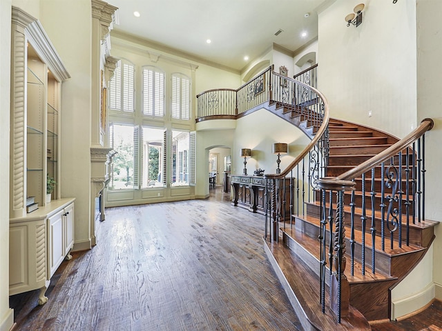 entryway with a towering ceiling, ornamental molding, and wood-type flooring