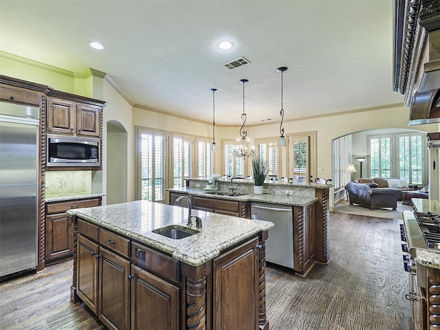 kitchen featuring sink, built in appliances, decorative light fixtures, a center island with sink, and dark hardwood / wood-style flooring