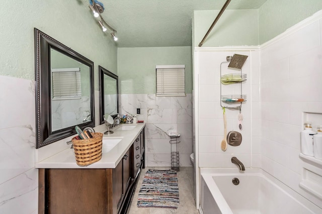 full bathroom with tile walls, tiled shower / bath combo, vanity, a textured ceiling, and toilet