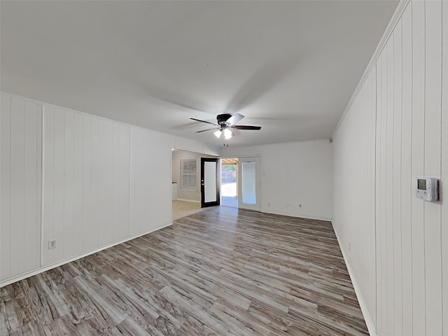 spare room with ceiling fan, wooden walls, and light hardwood / wood-style flooring