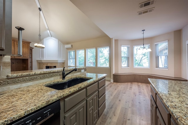 kitchen featuring sink, an inviting chandelier, black dishwasher, light hardwood / wood-style flooring, and light stone countertops