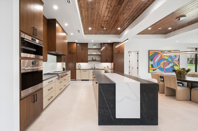 kitchen featuring a spacious island, a tray ceiling, stainless steel gas cooktop, wood ceiling, and dark stone counters