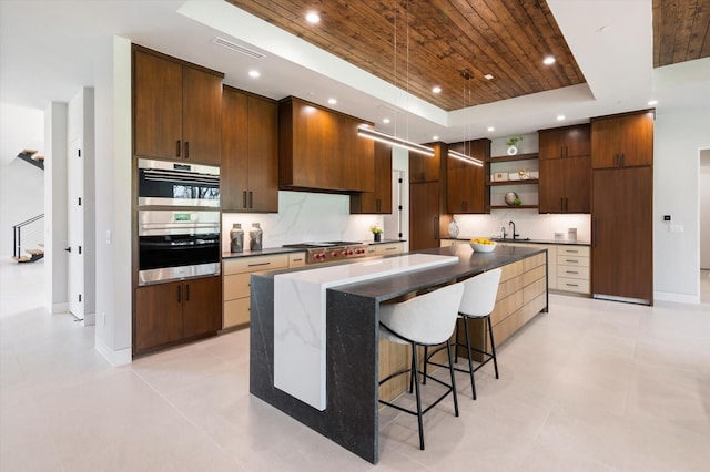 kitchen featuring a kitchen island, stainless steel appliances, sink, a raised ceiling, and a breakfast bar