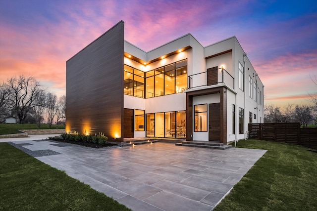 back house at dusk featuring a yard, a balcony, and a patio