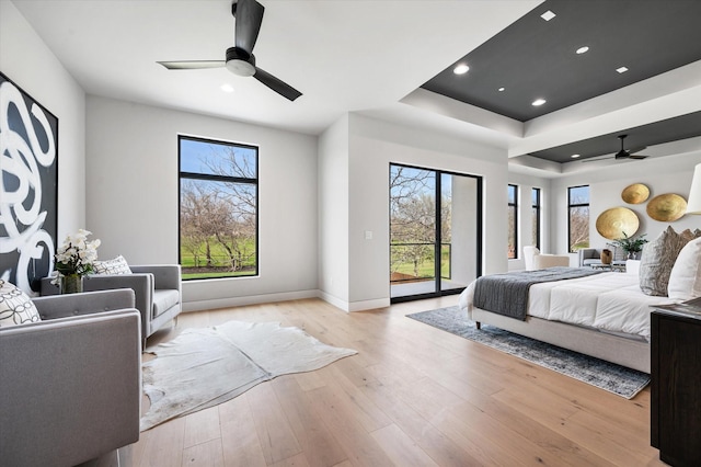 bedroom with ceiling fan, access to exterior, a tray ceiling, and light hardwood / wood-style floors