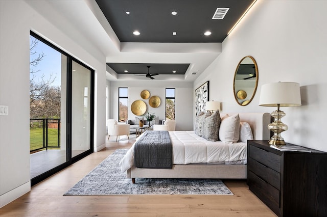 bedroom with access to exterior, a raised ceiling, and light wood-type flooring