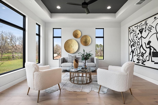 living area featuring ceiling fan, a healthy amount of sunlight, wood-type flooring, and a tray ceiling