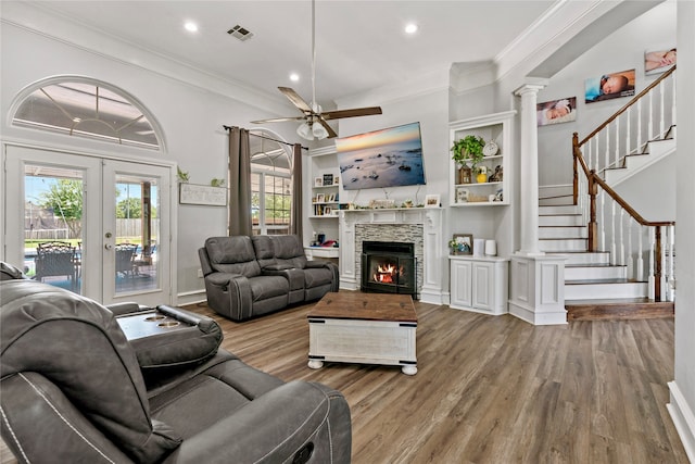 living room with hardwood / wood-style floors, a stone fireplace, french doors, ornate columns, and ceiling fan