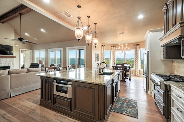 kitchen featuring appliances with stainless steel finishes, dark brown cabinetry, decorative light fixtures, and an island with sink