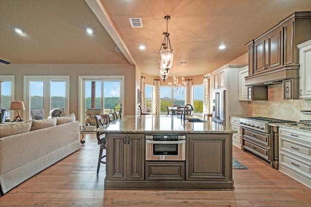 kitchen featuring sink, a kitchen island with sink, hanging light fixtures, stainless steel appliances, and a kitchen bar