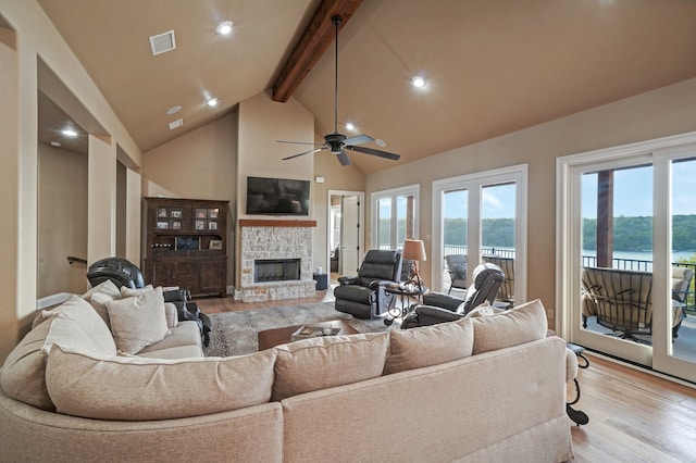 living room featuring a stone fireplace, light wood-type flooring, high vaulted ceiling, and beam ceiling