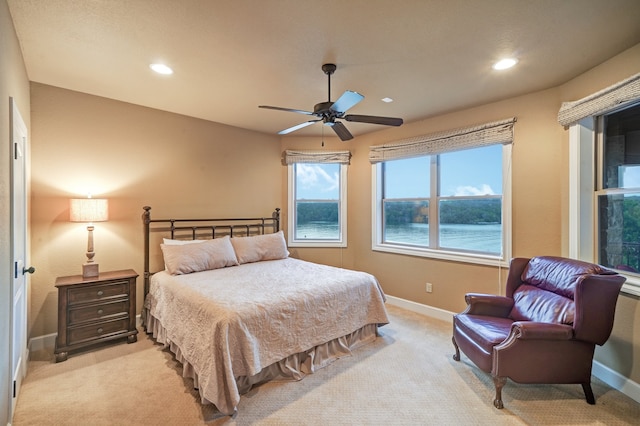 bedroom featuring light colored carpet, ceiling fan, and a water view