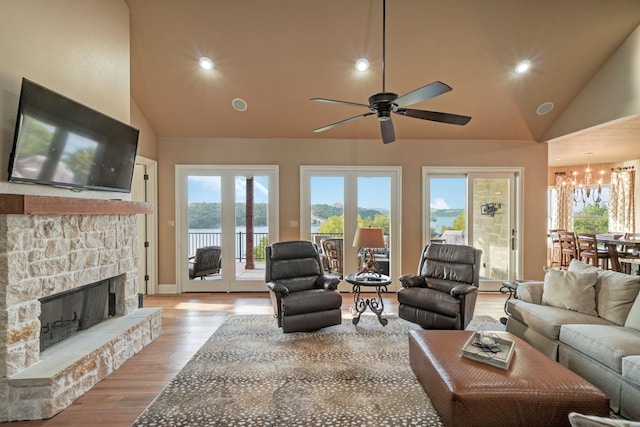 living room featuring high vaulted ceiling, ceiling fan with notable chandelier, a fireplace, and light wood-type flooring