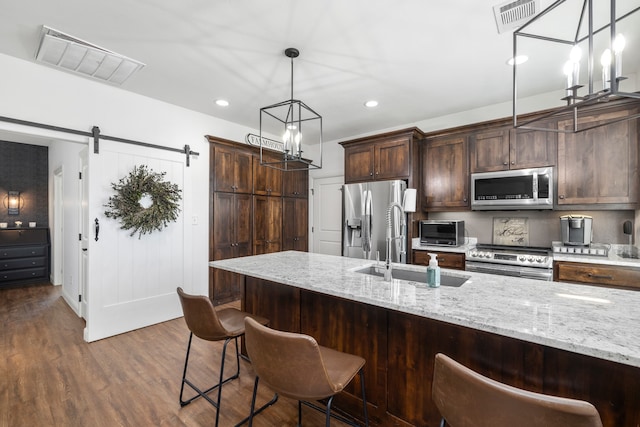 kitchen with dark wood-type flooring, sink, a barn door, light stone countertops, and appliances with stainless steel finishes