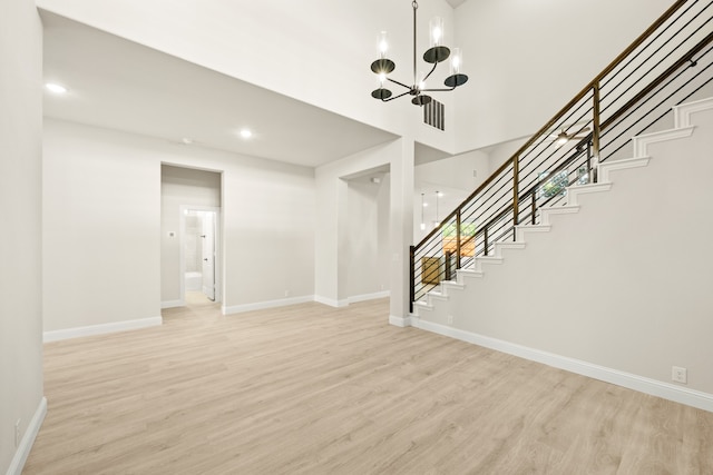 interior space with light hardwood / wood-style flooring, a towering ceiling, and a notable chandelier