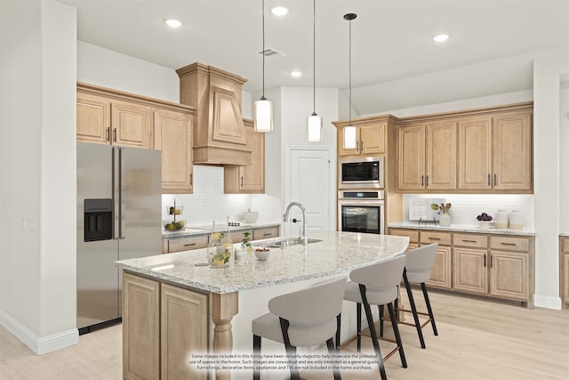 kitchen featuring sink, stainless steel appliances, light stone counters, light hardwood / wood-style floors, and a center island with sink