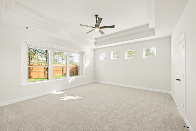 empty room with light carpet, a raised ceiling, and ceiling fan