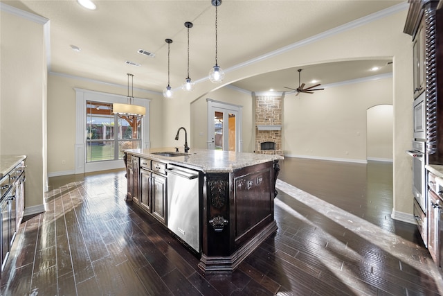 kitchen with appliances with stainless steel finishes, sink, a fireplace, an island with sink, and dark wood-type flooring