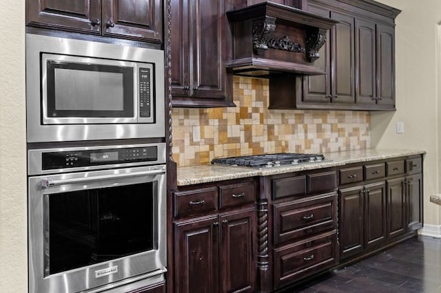 kitchen with dark hardwood / wood-style flooring, light stone counters, custom range hood, appliances with stainless steel finishes, and backsplash