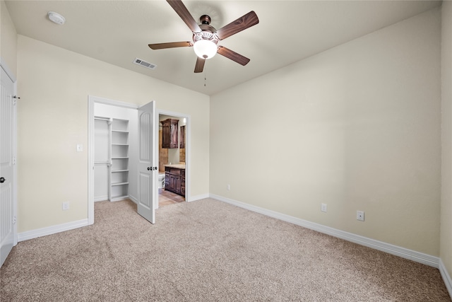 unfurnished bedroom featuring a closet, connected bathroom, ceiling fan, a walk in closet, and light colored carpet