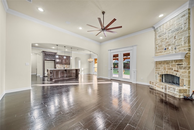 living room featuring ceiling fan, a stone fireplace, dark wood-type flooring, and ornamental molding