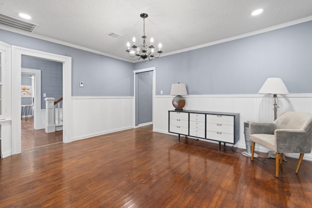 living area with wainscoting, visible vents, a textured ceiling, and hardwood / wood-style flooring