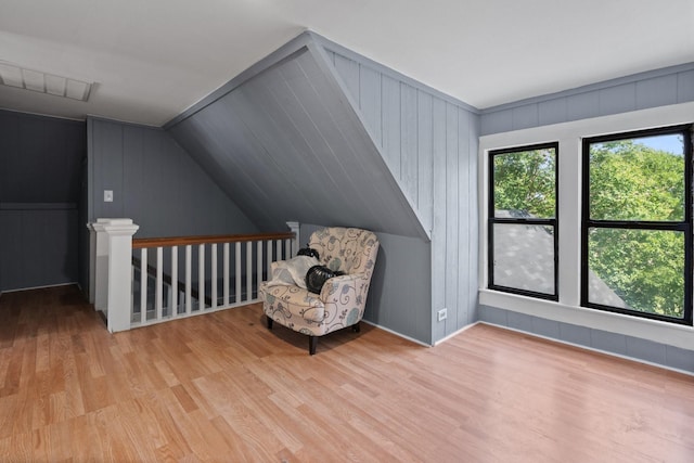 unfurnished room featuring lofted ceiling, visible vents, an upstairs landing, and wood finished floors