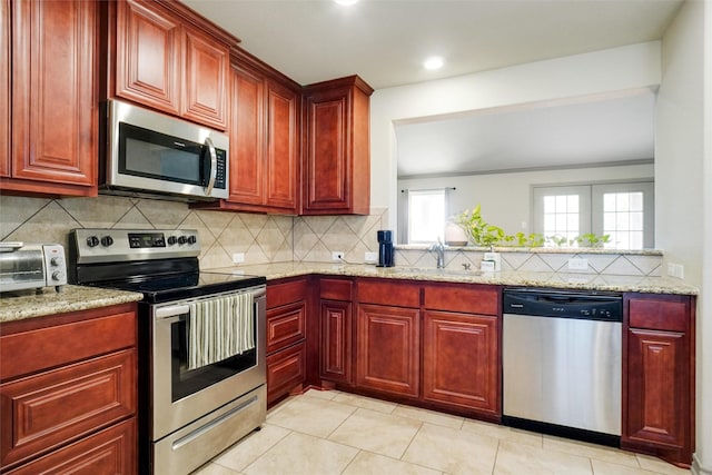 kitchen with appliances with stainless steel finishes, backsplash, light stone counters, sink, and light tile patterned floors