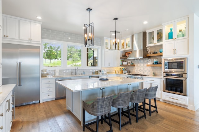 kitchen with a center island, light hardwood / wood-style flooring, wall chimney exhaust hood, and built in appliances