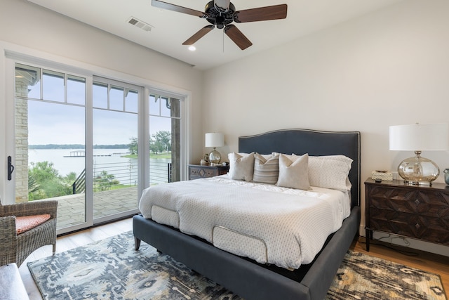 bedroom with multiple windows, a water view, and hardwood / wood-style flooring