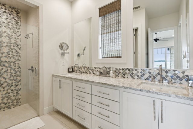 bathroom featuring ceiling fan, a tile shower, dual bowl vanity, tile patterned flooring, and backsplash