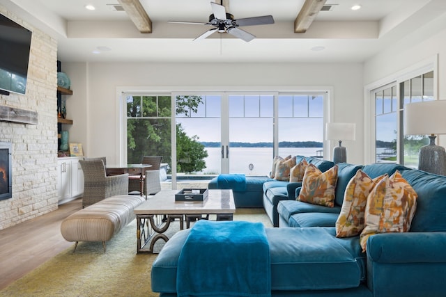 living room with a water view, ceiling fan, beamed ceiling, a fireplace, and wood-type flooring