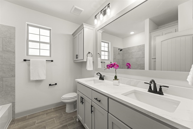 full bathroom featuring tiled shower / bath combo, plenty of natural light, vanity, and toilet