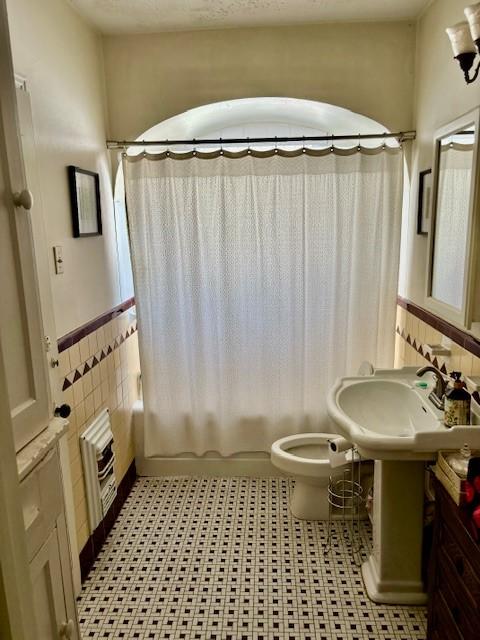 full bathroom featuring radiator heating unit, sink, tile walls, toilet, and shower / bath combo with shower curtain