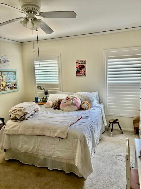 carpeted bedroom featuring multiple windows, crown molding, and ceiling fan