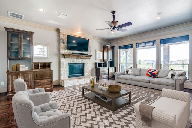 living room with ceiling fan, hardwood / wood-style floors, crown molding, and a stone fireplace