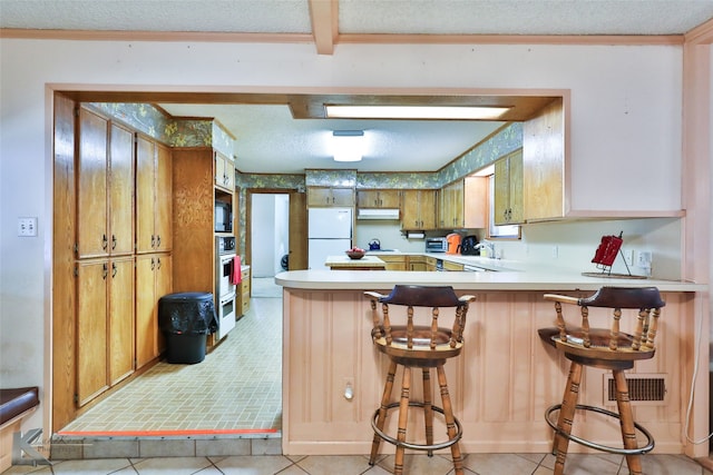 kitchen featuring a breakfast bar, white refrigerator, kitchen peninsula, and a textured ceiling