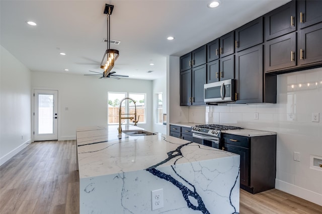 kitchen featuring ceiling fan, stainless steel appliances, light stone countertops, light hardwood / wood-style flooring, and backsplash