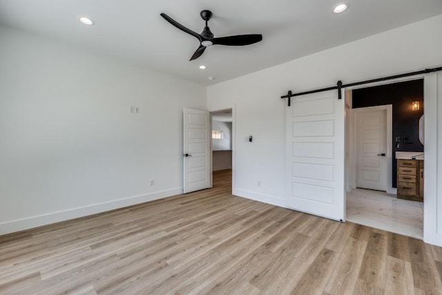 unfurnished bedroom with light hardwood / wood-style floors, ensuite bathroom, a barn door, and ceiling fan