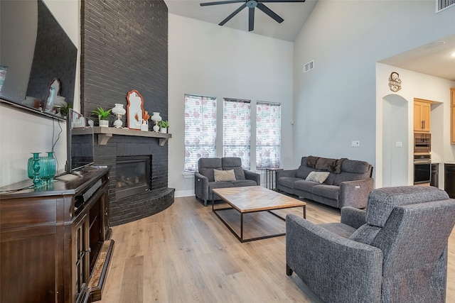 living room with ceiling fan, high vaulted ceiling, a brick fireplace, and light wood-type flooring