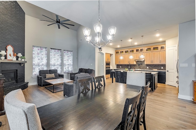 dining room with lofted ceiling, light hardwood / wood-style floors, ceiling fan with notable chandelier, and a brick fireplace