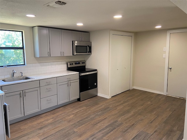 kitchen with appliances with stainless steel finishes, dark hardwood / wood-style flooring, tasteful backsplash, sink, and gray cabinets