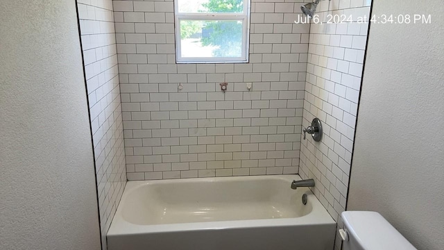 bathroom with tiled shower / bath combo and toilet