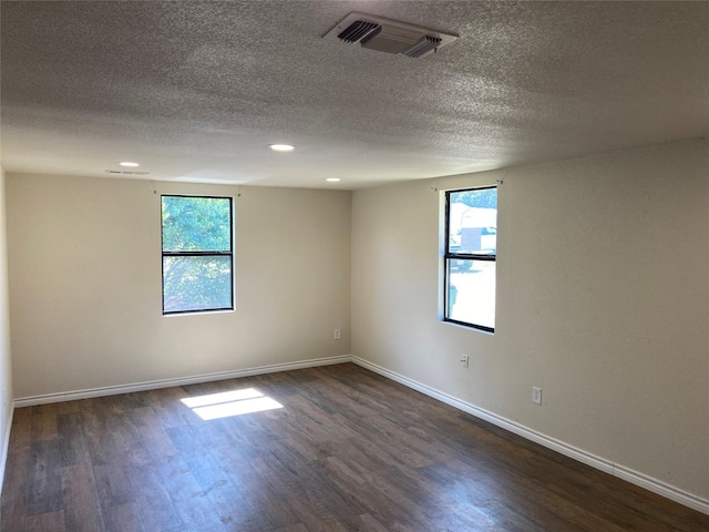 spare room featuring a textured ceiling, dark hardwood / wood-style floors, and a healthy amount of sunlight