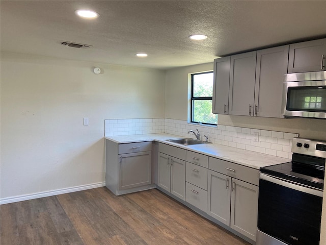 kitchen featuring light hardwood / wood-style flooring, sink, gray cabinets, decorative backsplash, and stainless steel appliances