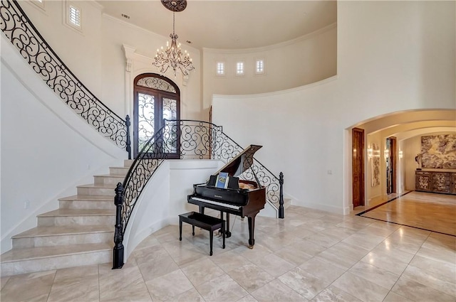 entrance foyer featuring arched walkways, a chandelier, a high ceiling, ornamental molding, and stairway