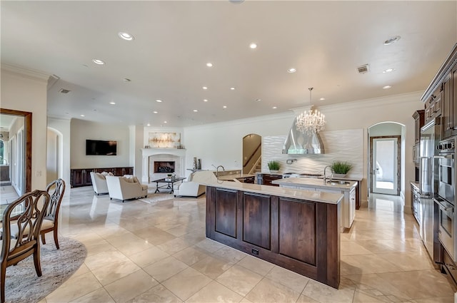 kitchen featuring a center island with sink, decorative light fixtures, dark brown cabinetry, decorative backsplash, and a chandelier