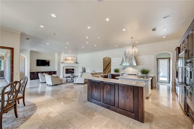 kitchen with an island with sink, a fireplace, dark brown cabinetry, and decorative light fixtures